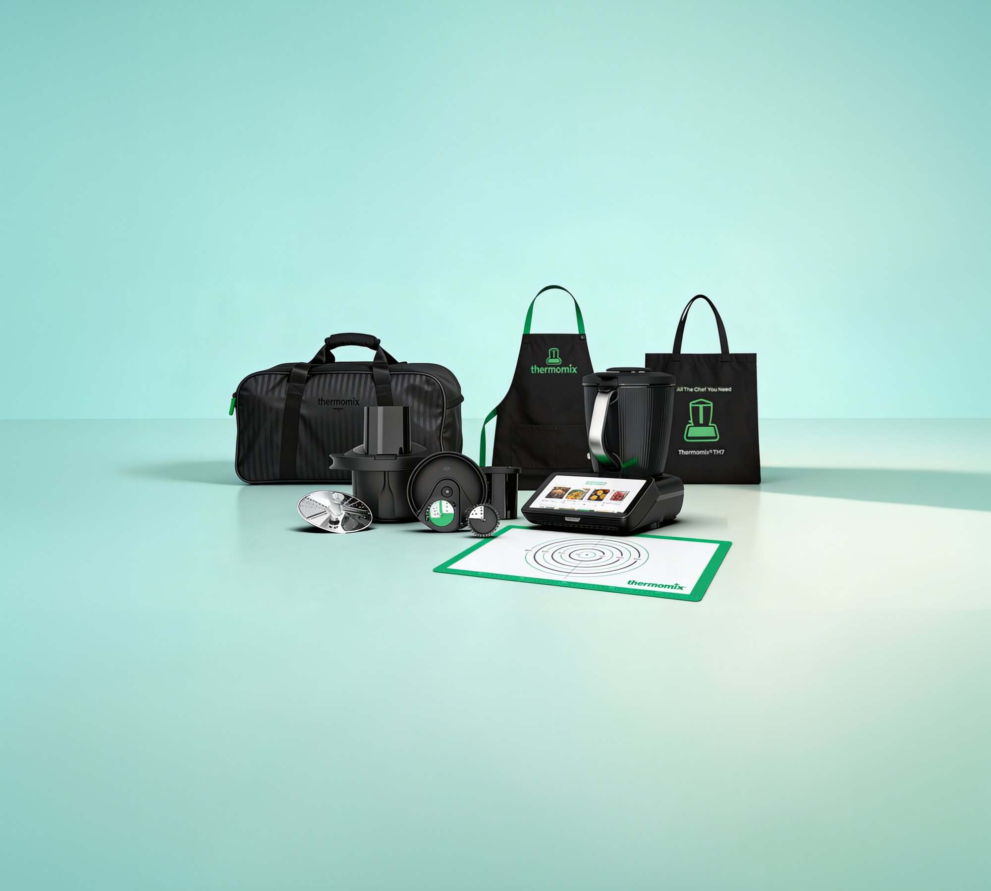 The Thermomix TM7 with its accessories, apron, tote and bag on a mint background